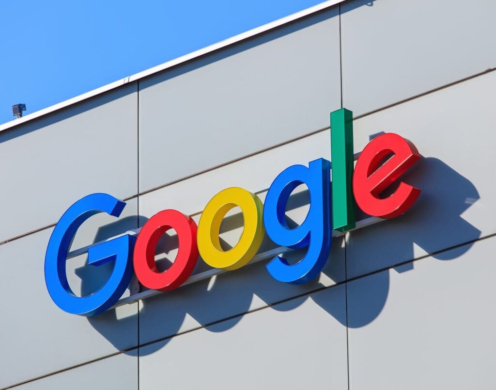 Image of a Google sign mounted on a sleek, modern building facade. The iconic multi-colored letters stand out against the neutral background, indicating the presence of a Google office or facility.